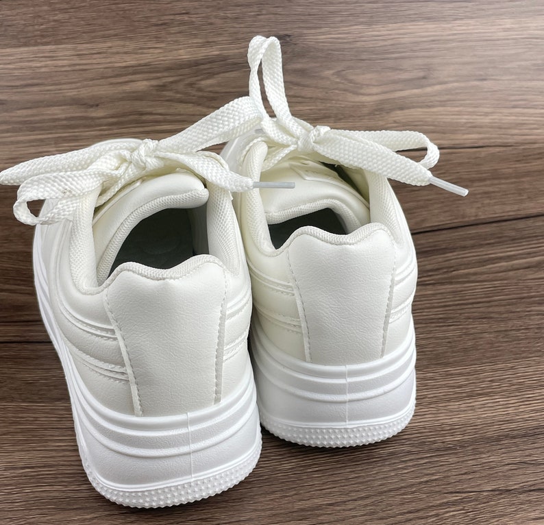 May include: A pair of white leather sneakers with white laces. The sneakers have a thick white sole and a rounded toe.