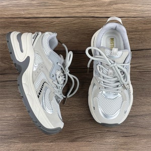 May include: A pair of grey and white trainers with a mesh upper and a chunky white sole. The trainers have a silver accent on the side and the word "Mister" is printed on the tongue.