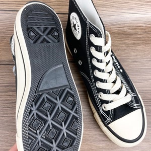 May include: Black high-top canvas sneakers with white laces and a white star logo on the side. The shoes have a black rubber sole with a diamond pattern.