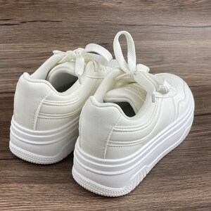 May include: A pair of white platform sneakers with a thick sole and laces. The sneakers have a simple design with a slightly textured upper.