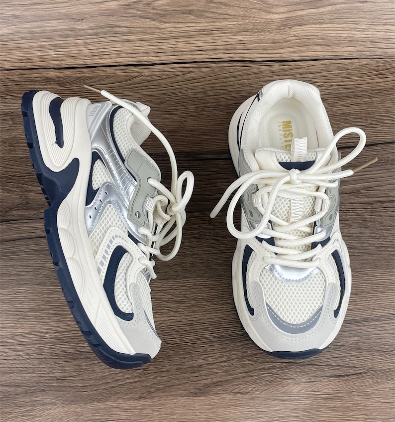 May include: A pair of white trainers with a silver mesh design and a chunky sole. The trainers have a navy blue trim and white laces.