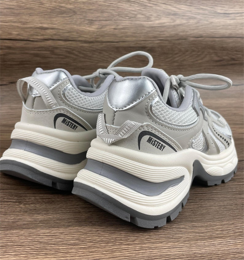 May include: A pair of grey and silver trainers with a chunky white sole. The trainers have a mesh upper and the word "MISTERY" is printed on the side of each shoe.