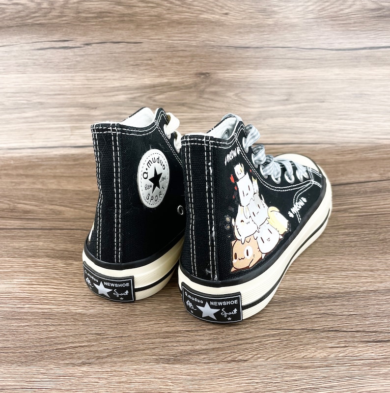May include: A pair of black high-top canvas sneakers with white stitching. One shoe features a black star with the text "a.mudao Sport" and the other shoe has a cartoon graphic of a stack of cute animals with the text "Know U" on the side.