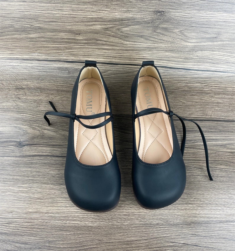 May include: A pair of black leather shoes with a lace-up design. The shoes have a rounded toe and a low heel. The brand name "TOMUL" is printed on the inside of each shoe.