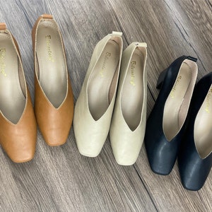 May include: Five pairs of women's shoes in different colours. The shoes are all pointed-toe flats with a v-shaped opening at the front. The shoes are in brown, beige, and black.
