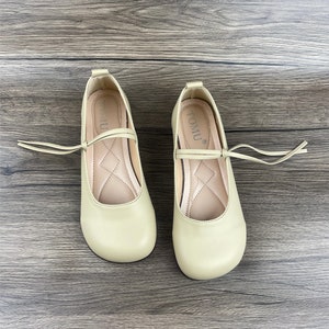 May include: A pair of light green ballet flats with a small bow and a tie at the ankle. The shoes have the word "TOMU" written on the inside.
