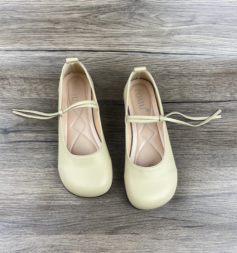 May include: A pair of light green ballet flats with a small bow and a tie at the ankle. The shoes have the word "TOMU" written on the inside.