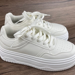 May include: White platform sneakers with white laces. The sneakers have a thick platform sole and a rounded toe.