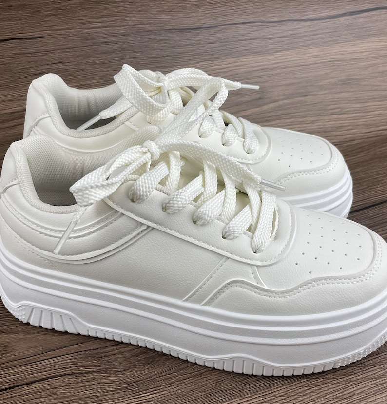 May include: White platform sneakers with white laces. The sneakers have a thick platform sole and a rounded toe.