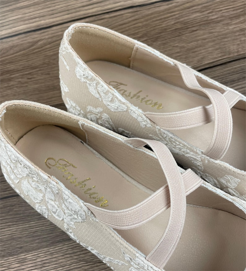 Może przedstawiać: Para beżowych but&oacute;w z pł&oacute;tna z białymi haftowanymi kwiatami i elastycznymi paskami. Buty mają napis "Fashion" wewnątrz.