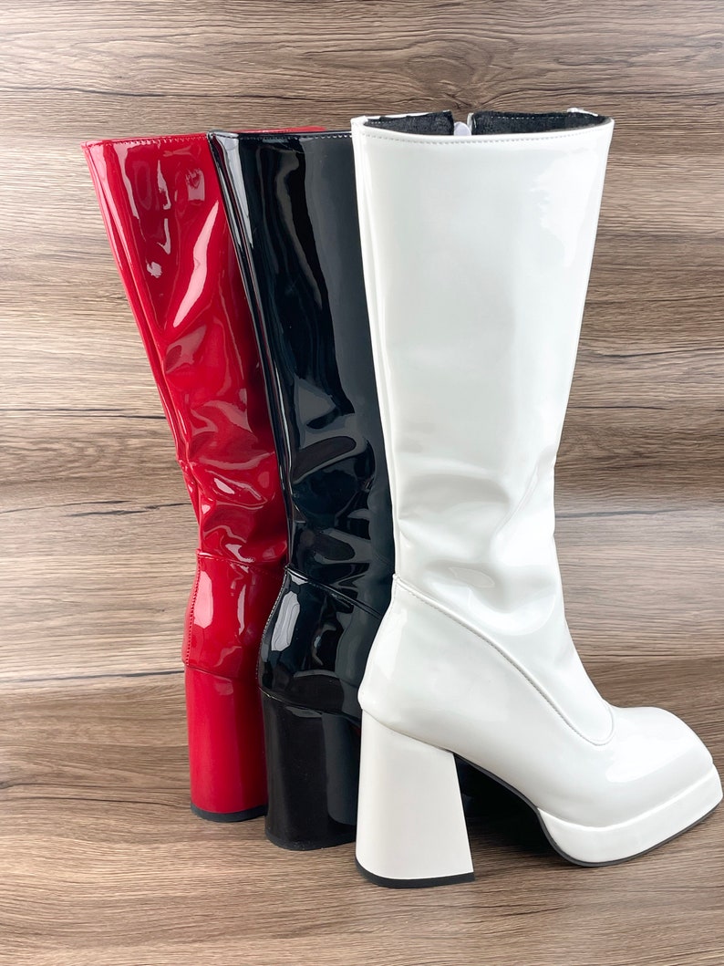 K&ouml;nnte beinhalten: Drei Paar kniehohe Stiefel in Rot, Schwarz und Wei&szlig;. Die Stiefel haben einen dicken Plateauabsatz und eine gl&auml;nzende Oberfl&auml;che.