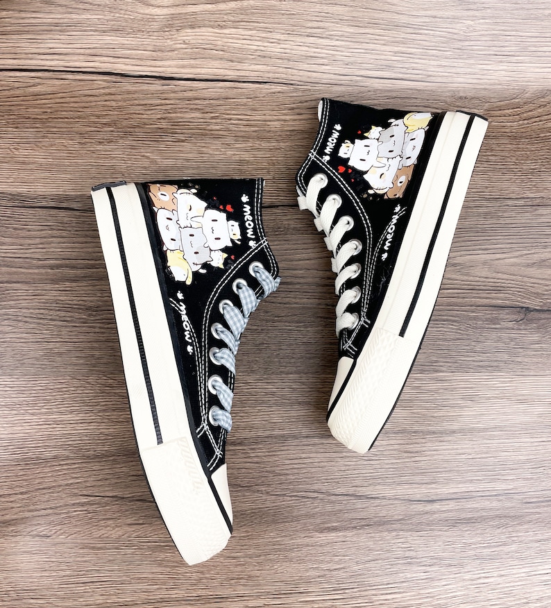 May include: A pair of black high-top canvas shoes with white soles. The shoes feature a cartoon print of cats with the word "meow" repeated on the sides.