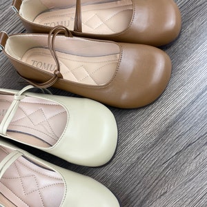 May include: Two pairs of women's shoes with a simple design. One pair is brown and the other pair is beige. Both pairs have a small bow on the front and a strap that goes around the ankle.