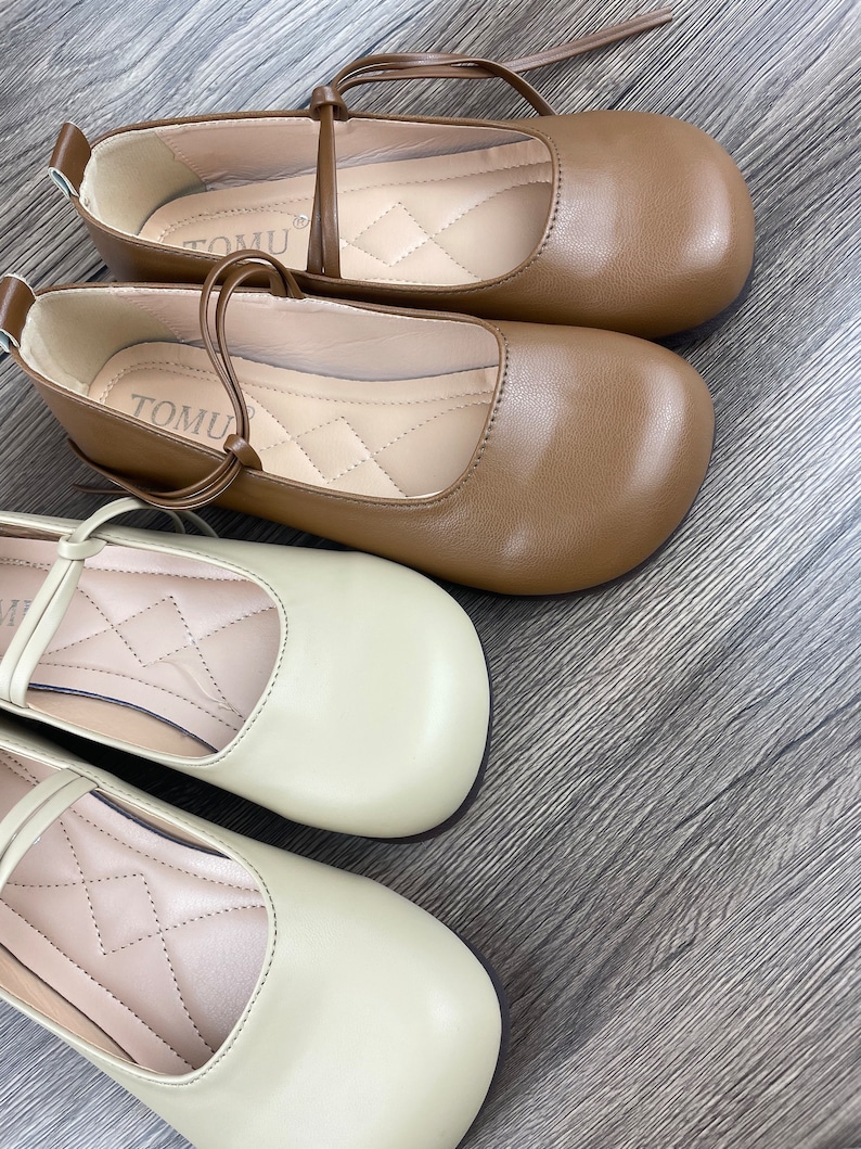May include: Two pairs of women's shoes with a simple design. One pair is brown and the other pair is beige. Both pairs have a small bow on the front and a strap that goes around the ankle.