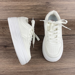 May include: A pair of white leather sneakers with white laces. The sneakers have a thick platform sole.