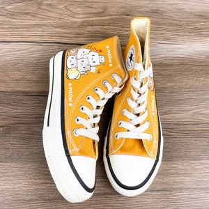 May include: A pair of yellow high-top canvas sneakers with a black trim. The sneakers feature a cartoon illustration of cats with the text "Meow" on each shoe.