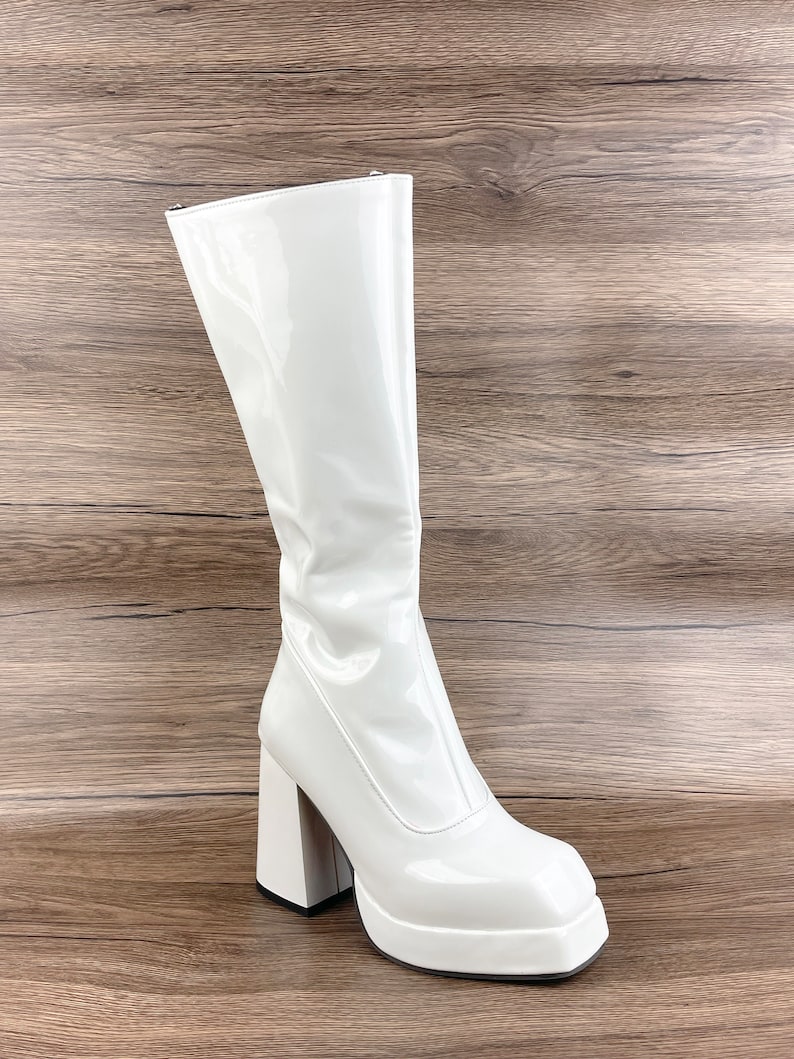 K&ouml;nnte beinhalten: Wei&szlig;e Lackleder-Plateau-Stiefeletten mit einem klobigeren Absatz. Die Stiefeletten haben eine quadratische Spitze und einen Rei&szlig;verschluss an der R&uuml;ckseite.