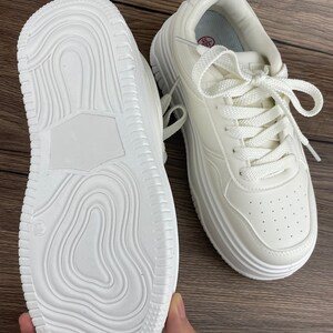 May include: A pair of white platform sneakers with white laces. The sneakers have a textured sole and a white leather upper.