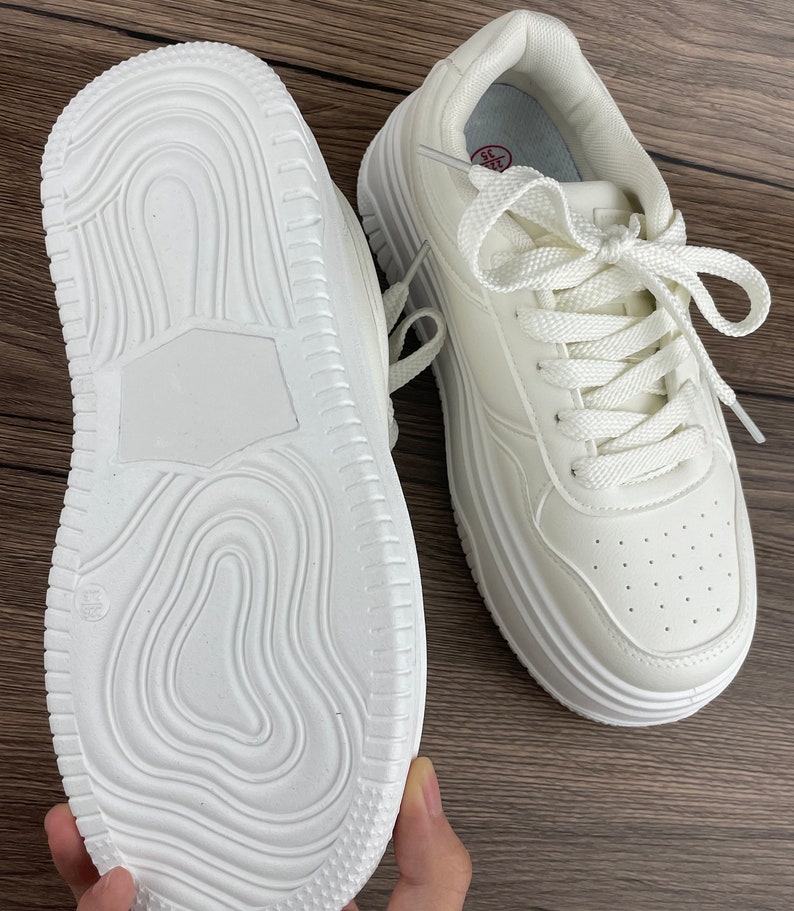 May include: A pair of white platform sneakers with white laces. The sneakers have a textured sole and a white leather upper.