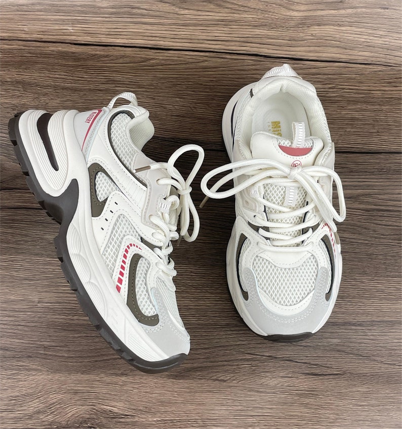 May include: A pair of white trainers with a mesh upper and a chunky sole. The trainers have a red and white stripe detail on the side and a white lace.