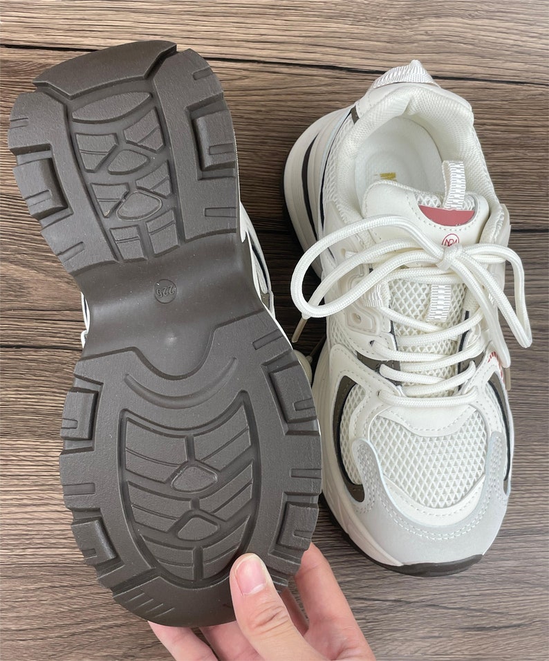 May include: White trainers with a brown rubber sole. The trainers have a mesh upper and a white lace-up closure.