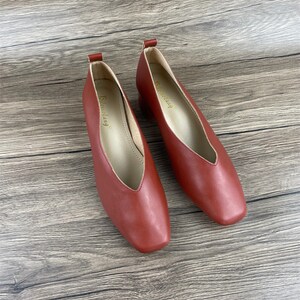 May include: A pair of red leather heeled shoes with a pointed toe and a v-shaped opening at the front. The shoes have a small block heel and the brand name "Strending" is printed on the inside of each shoe.