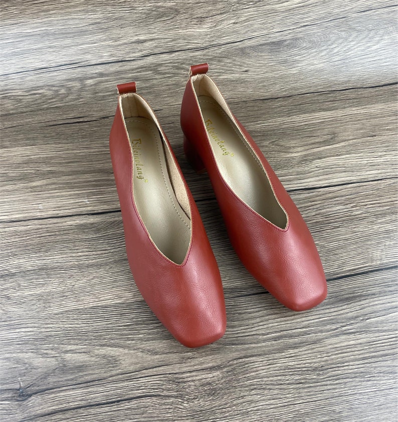 May include: A pair of red leather heeled shoes with a pointed toe and a v-shaped opening at the front. The shoes have a small block heel and the brand name "Strending" is printed on the inside of each shoe.