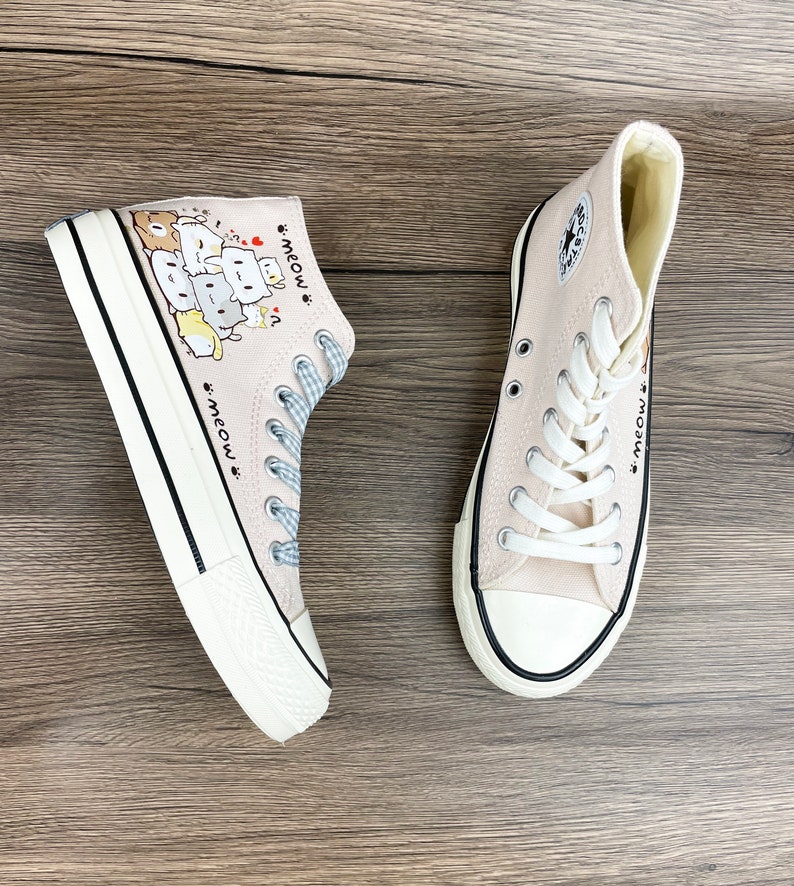 May include: A pair of light pink high-top canvas shoes with a black trim. The shoes have a cartoon design of cats stacked on top of each other with the text "meow" on the side.