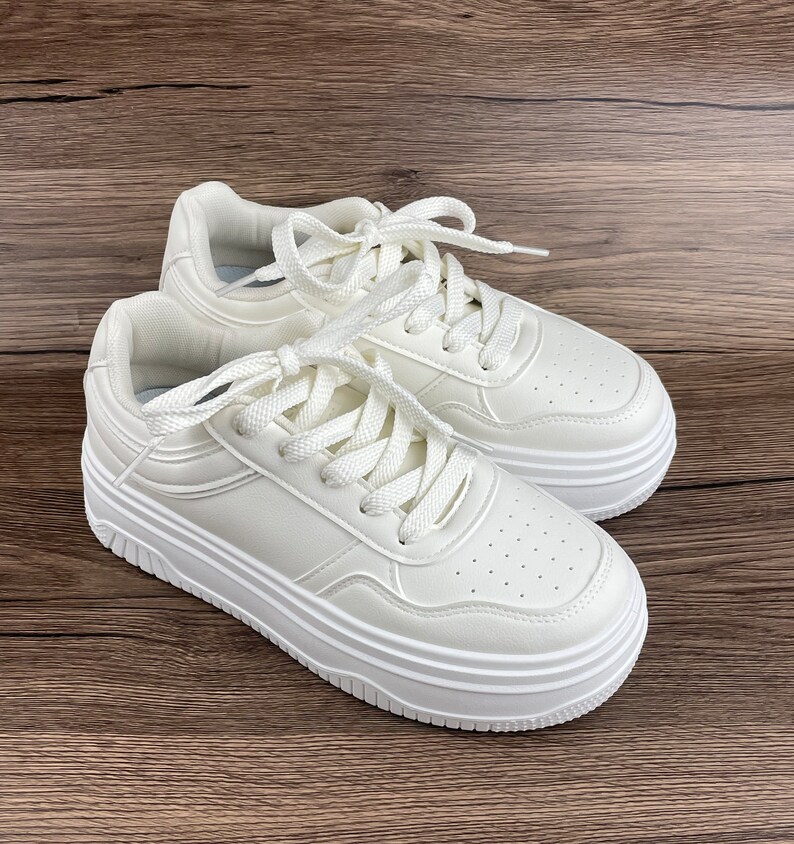 May include: A pair of white platform sneakers with white laces. The sneakers have a textured leather upper and a thick, multi-layered platform sole.