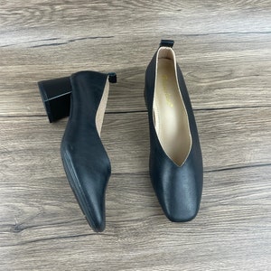 May include: A pair of black leather heeled shoes with a square toe. The shoes have a low block heel and a pointed vamp.