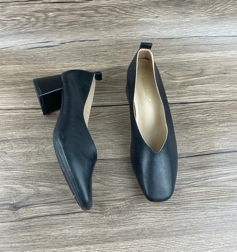 May include: A pair of black leather heeled shoes with a square toe. The shoes have a low block heel and a pointed vamp.