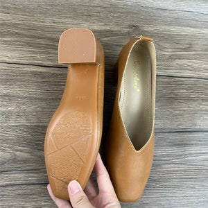 May include: A pair of brown leather heeled shoes with a pointed toe. The shoes have a low heel and a simple design. The brand name "Taisenwang" is printed on the inside of one shoe.