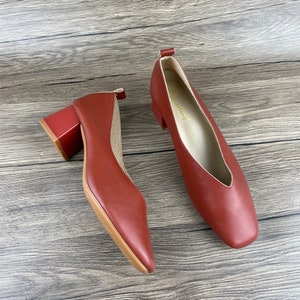 May include: A pair of red leather heeled shoes with a square toe and a block heel. The shoes have a gold label on the inside that says "Fashionlady".