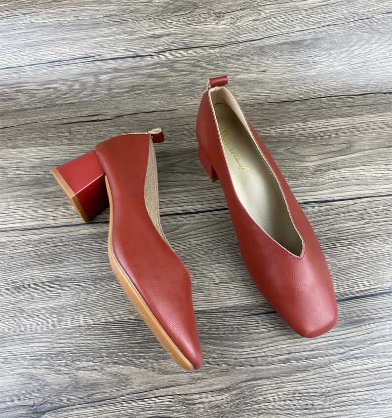 May include: A pair of red leather heeled shoes with a square toe and a block heel. The shoes have a gold label on the inside that says "Fashionlady".