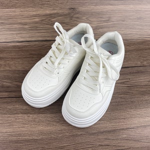 May include: A pair of white platform sneakers with white laces. The sneakers have a thick, chunky sole and a rounded toe.