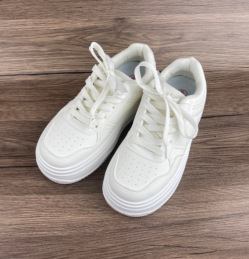 May include: A pair of white platform sneakers with white laces. The sneakers have a thick, chunky sole and a rounded toe.