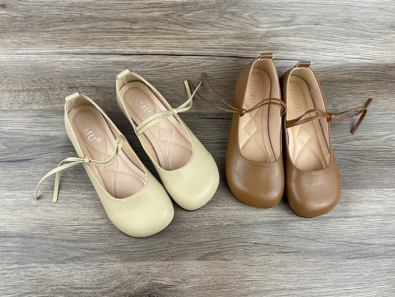 May include: Two pairs of beige and brown ballet flats with a ribbon tie. The shoes have a rounded toe and a low heel.