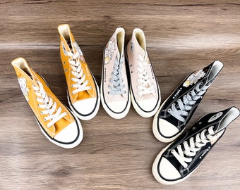 Puede incluir: Cuatro pares de zapatillas de lona de caña alta con diseños de personajes de dibujos animados. Las zapatillas son de color amarillo, beige, negro y blanco.