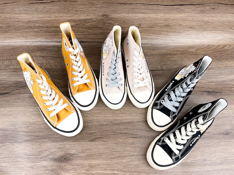 May include: Four pairs of high-top canvas sneakers with cartoon character designs. The sneakers are in yellow, beige, black, and white.