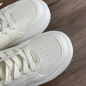 May include: A pair of white leather sneakers with white laces. The sneakers have a thick white sole and are made of a breathable material.