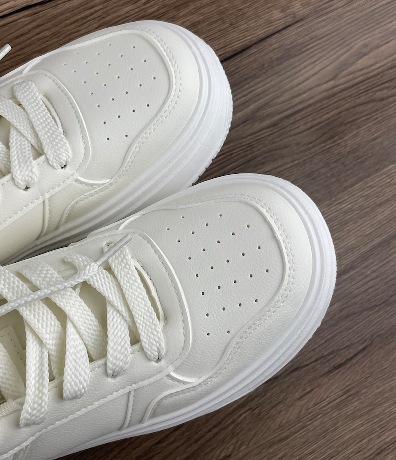 May include: A pair of white leather sneakers with white laces. The sneakers have a thick white sole and are made of a breathable material.