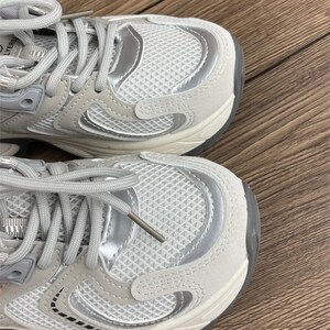 May include: A pair of white trainers with silver accents. The trainers have a chunky sole and a mesh upper.