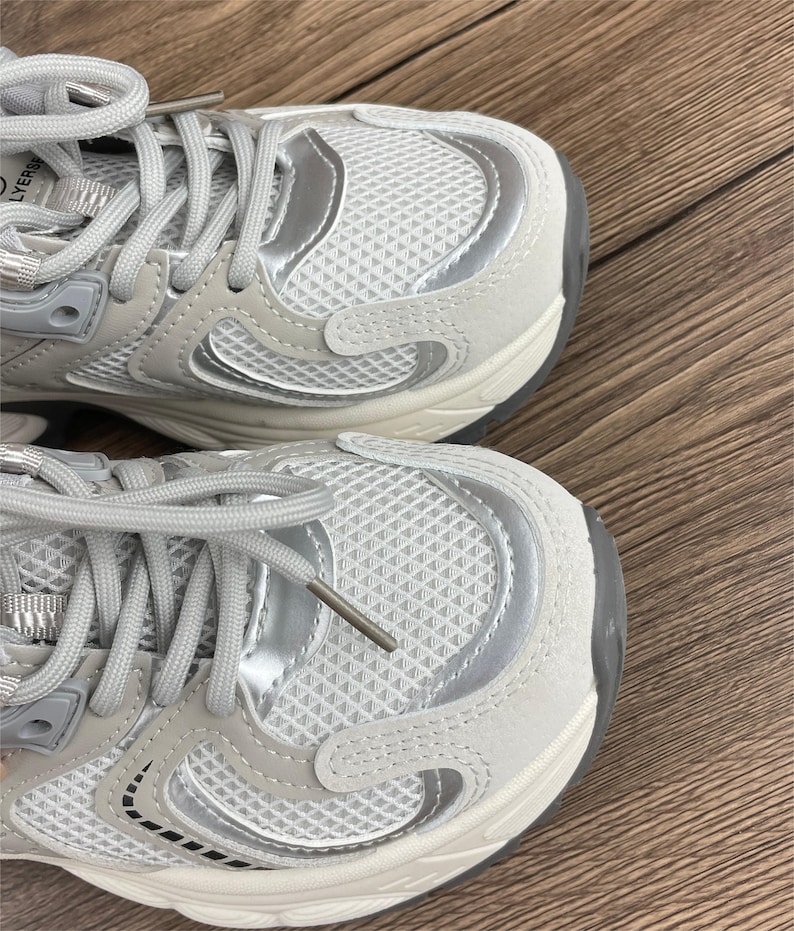 May include: A pair of white trainers with silver accents. The trainers have a chunky sole and a mesh upper.