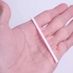 May include: A white plastic yarn needle with a rounded tip and a large eye. The needle is held in a hand, showcasing its size and design. Ideal for various crafts, including knitting and crochet.