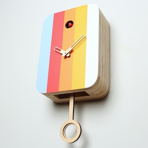 May include: A colorful cuckoo clock with a rainbow design. The clock face features vertical stripes in blue, red, orange, yellow, and white. The clock has a wooden pendulum and hands. The clock is mounted on a white wall.