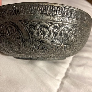 Può includere: Una ciotola in metallo argentato con intricati disegni in rilievo. La ciotola ha una forma circolare e un bordo leggermente svasato.