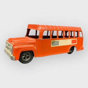 Może przedstawiać: Zabytkowy pomarańczowy szkolny autobus zabawkowy z czarnymi kołami i srebrnym przednim grillem. Autobus ma biały i żółty prostokątny obszar z boku i czerwony kwadrat. Autobus ma klasyczny design.