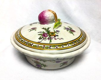 May include: A white porcelain dish with a lid. The lid is decorated with a pink and green fruit and floral design. The dish is decorated with a yellow and green floral design.
