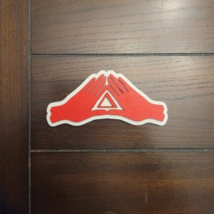 May include: A red paper cutout of two hands forming a triangle shape. The hands are white with red outlines and the triangle is red.