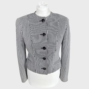 May include: A black and white striped blazer with a mandarin collar and four black buttons. The jacket has a tailored fit and two small pockets. The vertical stripes create a slimming effect. The blazer is displayed on a white mannequin.
